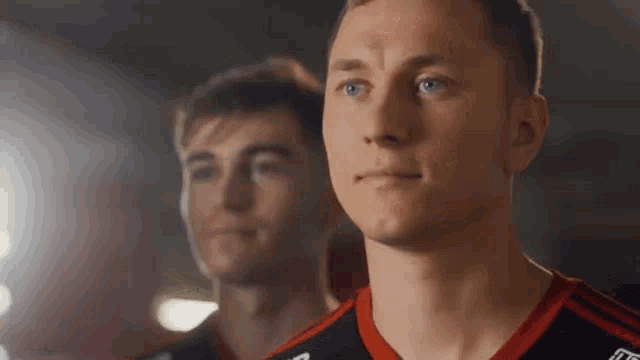two men are standing next to each other in a dark room . one of the men is wearing a nike shirt .