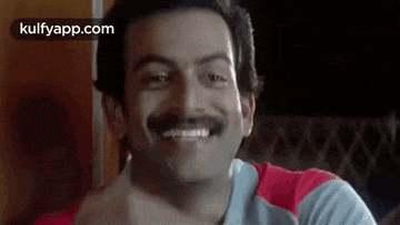 a man with a mustache is smiling while sitting at a table .