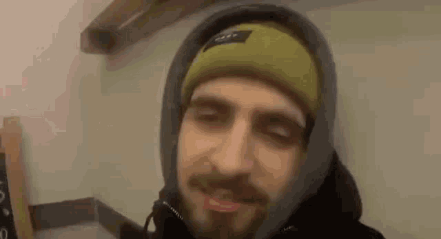 a man with a beard wearing a hooded jacket and a green beanie .