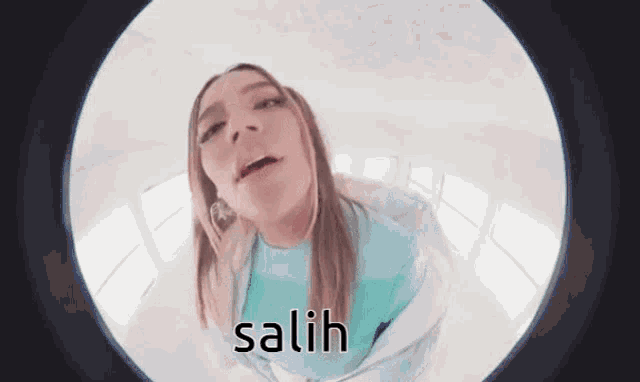 a woman in a blue shirt is looking through a fisheye lens and the word salih is on the screen