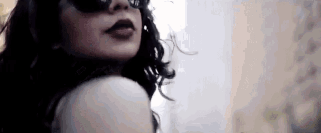 a woman wearing sunglasses and lipstick is looking over her shoulder at the camera .