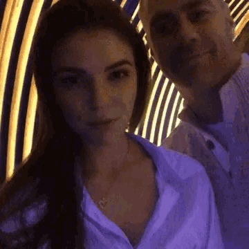 a man and a woman are posing for a picture in front of a purple wall .