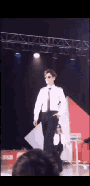 a man in a white shirt and black tie is walking on a stage in front of a crowd .