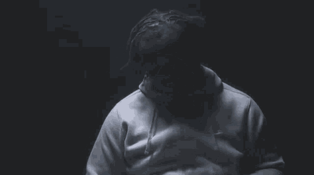 a man in a white hoodie is standing in the dark .
