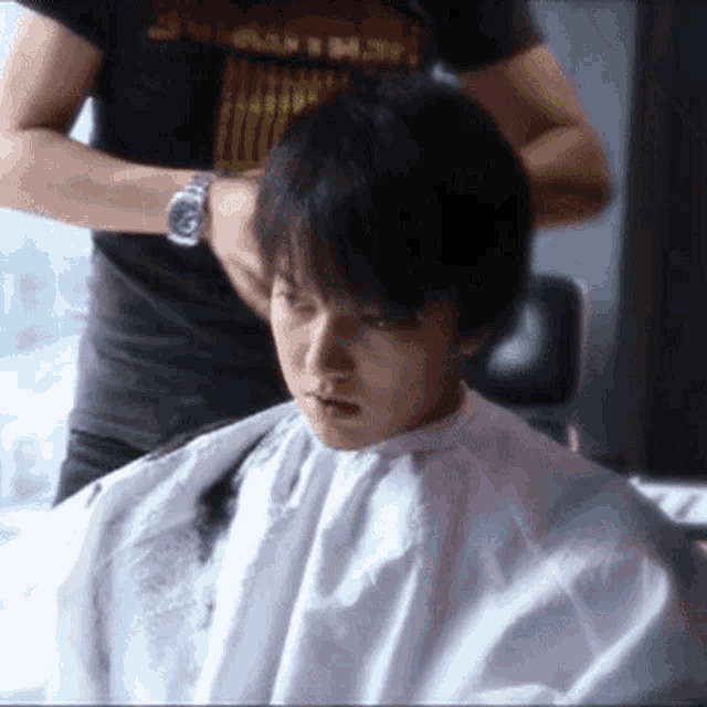 a man is getting his hair cut by a person wearing a watch