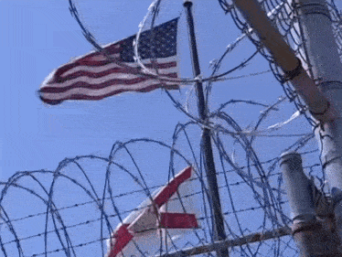 a barbed wire fence with an american flag behind it