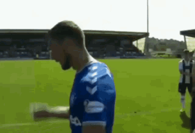 a man in a blue shirt is standing on a soccer field with his arms outstretched .