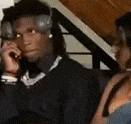 a man wearing headphones is talking on a cell phone while a woman watches .