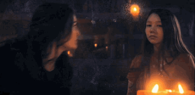 a woman is holding a candle in front of a girl in a dark room