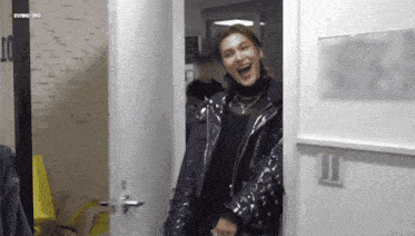 a woman in a black jacket is standing in a doorway laughing .