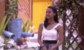 a woman in a white tank top is standing next to a blue watering can in a garden .
