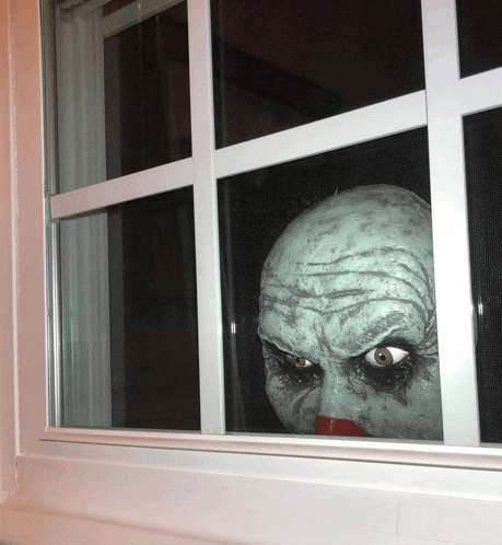 a scary clown looking out of a window with a red nose