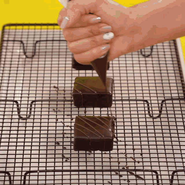 a person is icing chocolate squares on a rack