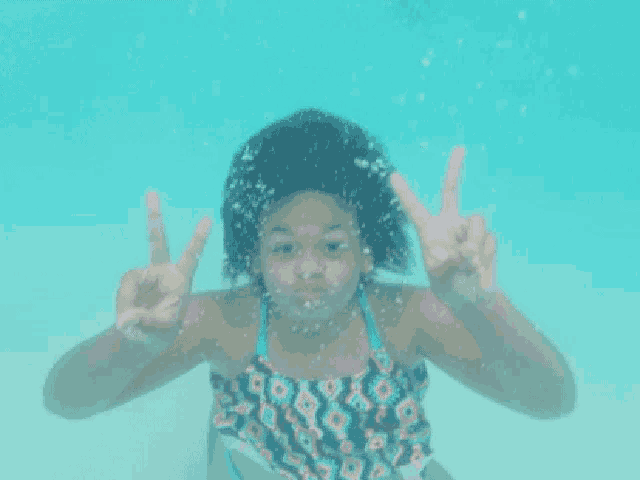 a little girl in a bathing suit is swimming underwater and giving the peace sign