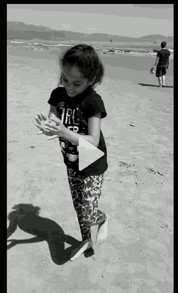 a girl wearing a girl power shirt is dancing on the beach .