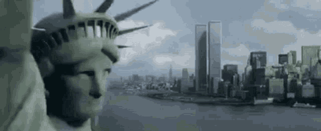 the statue of liberty is standing in front of a city skyline with two twin towers in the background .