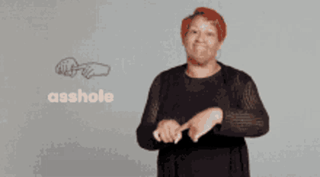 a woman with red hair is making a sign that says " asshole "