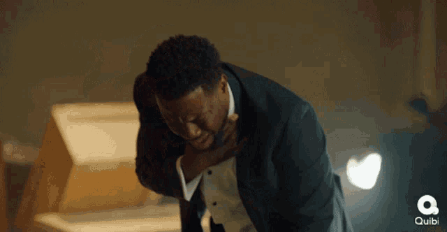a man in a tuxedo is holding his chest in pain and the word quibi is visible in the background