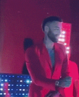 a man in a red jacket is singing into a microphone on a stage