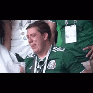 a man in a green soccer jersey is crying while sitting in the stands .