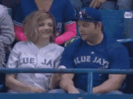a man wearing a blue jays jersey looks at a woman