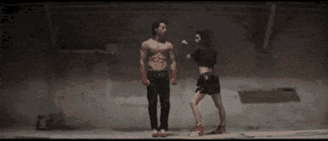 a man and a woman are dancing in a dark room . the woman is wearing red boxing gloves .