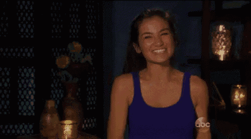 a woman in a blue tank top is laughing and dancing in a dark room .