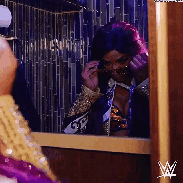 a woman adjusts her sunglasses in front of a mirror with a w logo on the wall