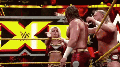 a group of wrestlers are standing in a wrestling ring with a woman standing next to them .