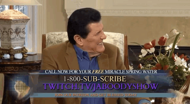 a man in a suit sits in a chair with a sign that says call now for your free miracle spring water 1-800-sub-scribe