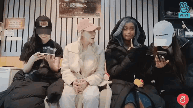 a group of women sitting next to each other looking at their cell phones with a vlive logo in the corner