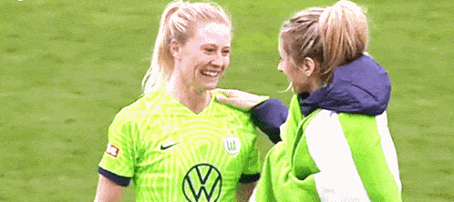 two female soccer players are standing next to each other on a field .