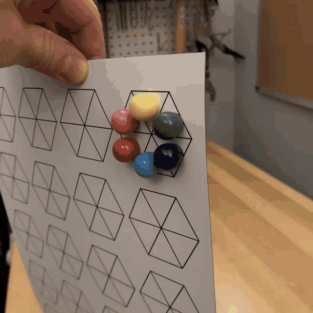 a person is holding a piece of paper with geometric shapes and crayons on it