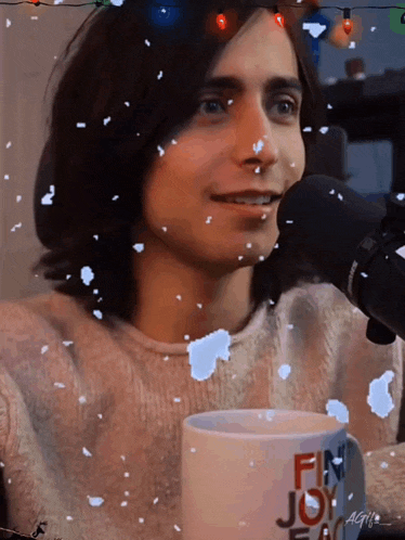a man in a pink sweater is sitting in front of a microphone and holding a mug that says fin joy