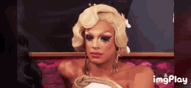 a drag queen is sitting in a chair with a flower in her hair and a caption that says imgplay
