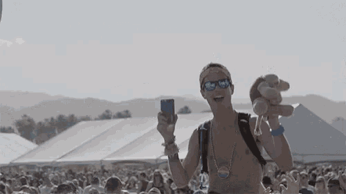 a shirtless man is holding a teddy bear and taking a picture of himself at a festival .