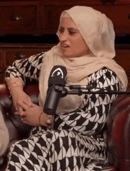 a woman wearing a hijab is sitting on a couch in front of a microphone .