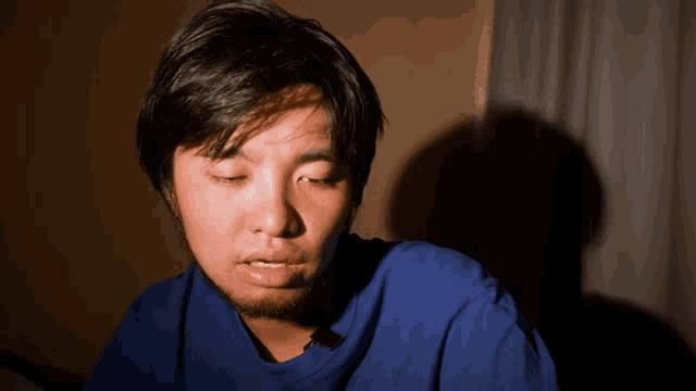 a man in a blue shirt has his eyes closed and a shadow on the wall behind him