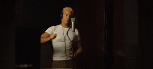 a man in a white shirt is singing into a microphone while wearing headphones .