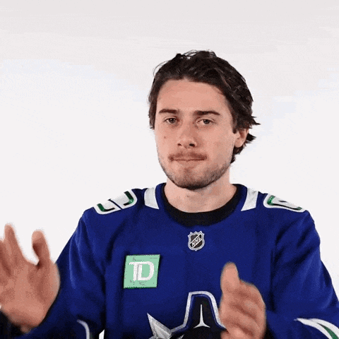 a man in a blue hockey jersey is clapping his hands in front of a white background .