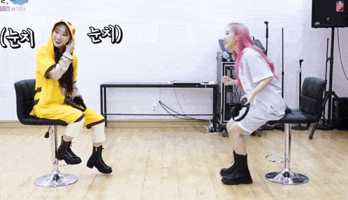 a girl with pink hair is sitting on a stool next to a girl in a yellow outfit
