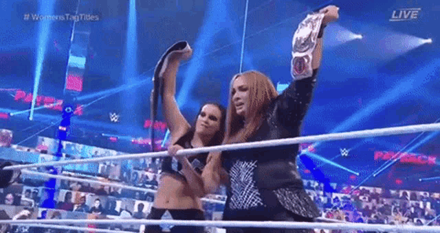 a couple of women are standing in a wrestling ring holding a championship belt .