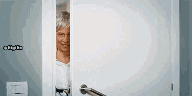 an elderly woman is peeking out of a door with a sticker on the wall that says gigigx