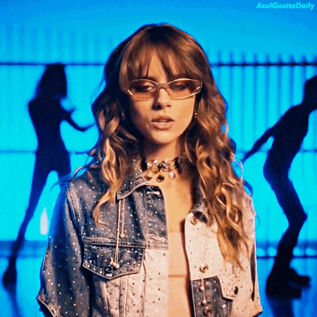 a woman wearing glasses and a denim jacket is standing in front of a blue background with the hashtag azulguaitedelly