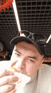 a man wearing a hat and sunglasses is eating a hamburger