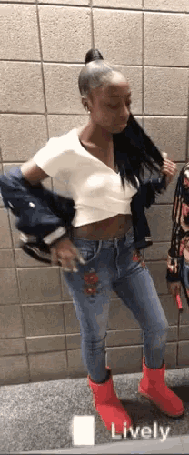 a woman in a white crop top and blue jeans is standing in front of a wall .