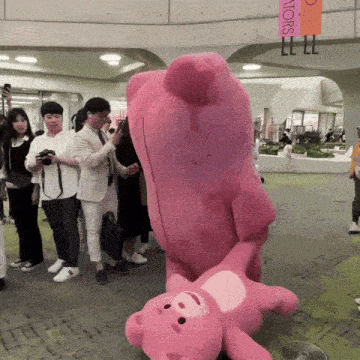 a group of people are standing around a large pink teddy bear with a sign that says ' i love you ' on it
