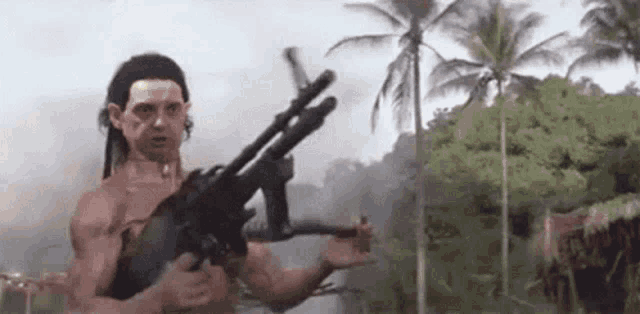 a man without a shirt is holding a gun in a jungle .