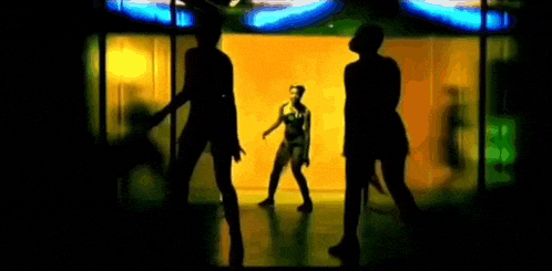 a woman is dancing in front of a yellow background with two other women standing behind her .