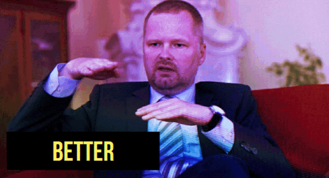 a man in a suit and tie is sitting on a red couch with the word better in yellow letters
